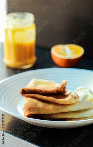 Thin Pancakes on the white plate with Orange Curd Jar on dark background and a half of orange vertical orientation