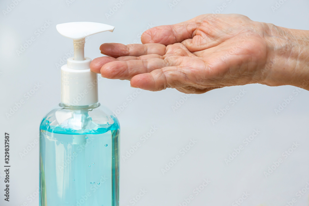 Senior woman's hand is using bottle of sanitizer gel pump dispenser to wash her hands in grey background. Close up & Macro shot, Select focus, Prevention from covid19, Bacteria, healthcare concept Senior woman's hand is using bottle of sanitizer gel pump dispenser to wash her hands in grey background. Close up & Macro shot, Select focus, Prevention from covid19, Bacteria, healthcare concept