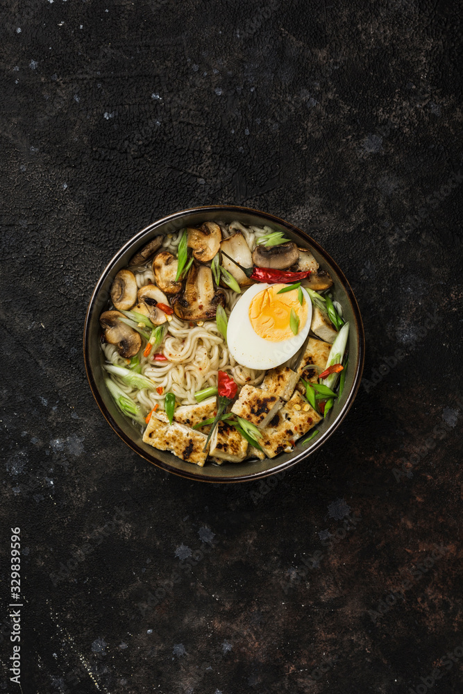 Noodle bowl with mushrooms, egg and tofu cheese on a dark background. Asian food. Noodle bowl with mushrooms, egg and tofu cheese on a dark background. Asian food.