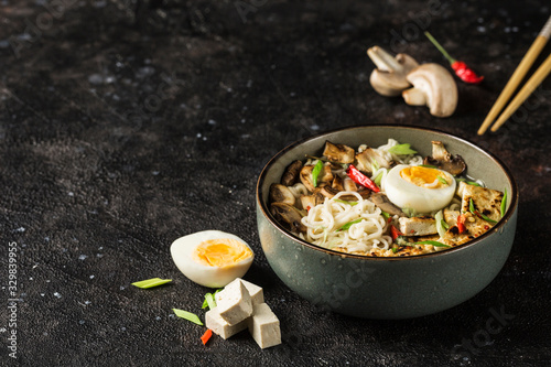 Noodle bowl with mushrooms, egg, tofu cheese, chopsticks and ingredients on a dark background. Asian food.