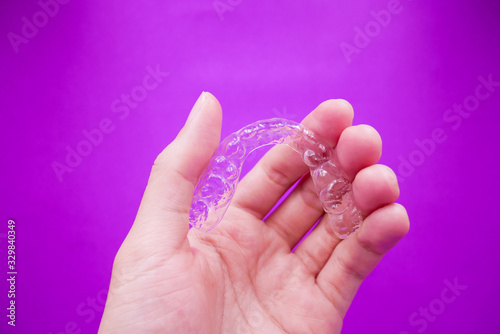 hand holding clear plastic retainer teeth that isolated on purple  background. it's an equipment for orthodontist give the patient to orthodontic surgery in dental clinic or hospital
