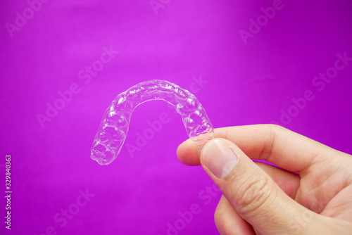 hand holding clear plastic retainer teeth that isolated on purple  background. it's an equipment for orthodontist give the patient to orthodontic surgery in dental clinic or hospital