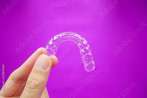 hand holding clear plastic retainer teeth that isolated on purple  background. it's an equipment for orthodontist give the patient to orthodontic surgery in dental clinic or hospital