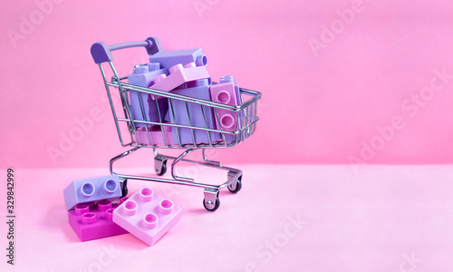 Close up of supermarket grocery push cart for shopping on pink background. Monochrome concept of buying games and toys for children. Copy space for advertisement