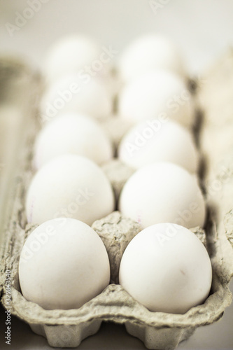 Several raw white eggs in the cardboard box on the table