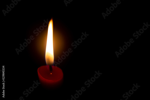 Red candle with yellow flame on black background