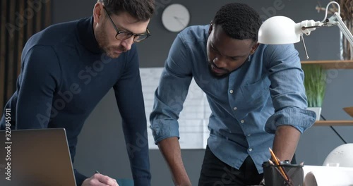 Two professional Architects go over blueprints in industrial Office, discussing. Experienced Creative Designer and Engineer Works with Afro-American Architect in Loft Office. Engineering. Architects. photo