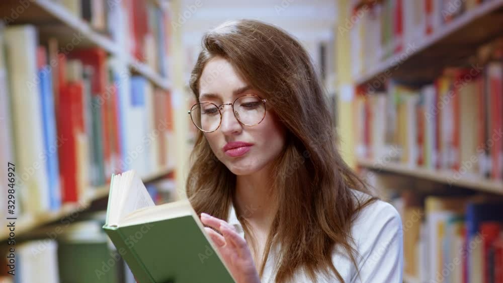 Portrait of smart attractive student young woman studying research reading a book searching information staying in modern library. Background of bookshelves. Portrait of smart attractive student young woman studying research reading a book searching information staying in modern library. Background of bookshelves.