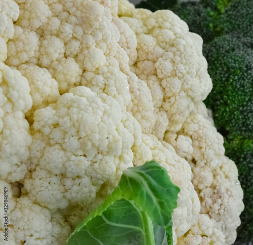 Closeup of a beautiful fresh cauliflower with green leaves next to a broccoli