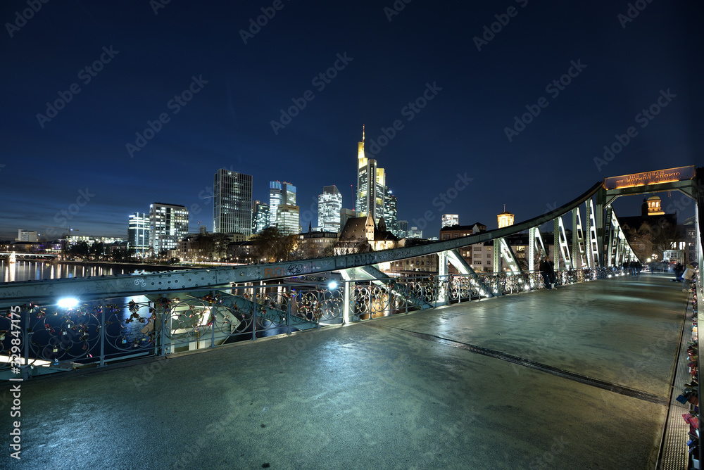 Obraz premium Der eiserne Steg in Frankfurt mit den Hochhäuser in der Nacht