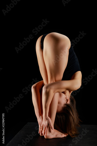 woman with barefoot doing forward bend exercise while practicing yoga isolated on black