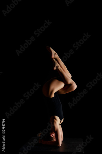 girl in bodysuit doing eagle legs handstand exercise isolated on black