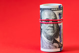 roll of 100 dollar banknotes on red background