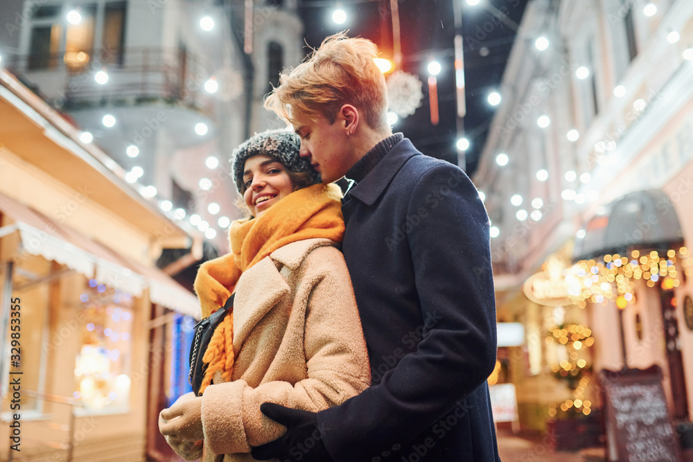 Closeness of the people. Happy young couple in warm clothes is on christmas decorated street together Closeness of the people. Happy young couple in warm clothes is on christmas decorated street together