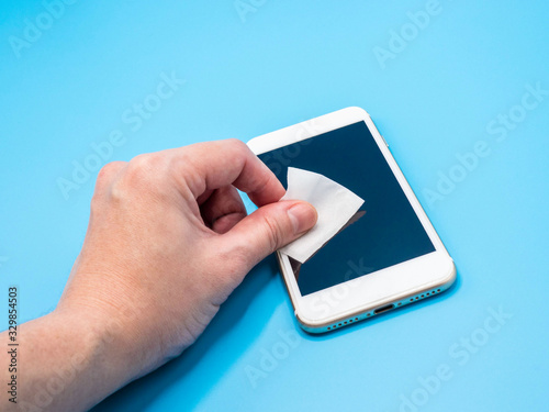 Asian women are wiping smartphone screen with alcohol pad to clean dust and germs preventing contamination from coronavirus. Hygiene and healthcare concept.
