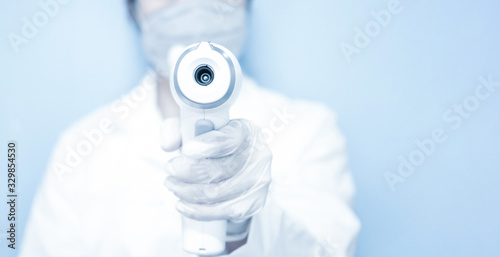 Woman doctor wearing mask and holding medical infrared forehead thermometer to check body temperature for virus symptoms. .Initial screening to prevent the coronavirus outbreak. Healthcare concept.