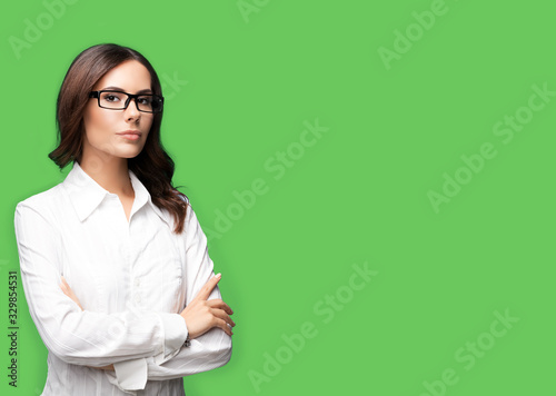 Portrait of seriously looking young businesswoman in glasses, with copy space for some slogan or text, over green color background. Success in business concept. photo