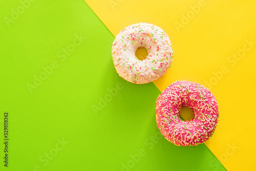 Colorful donuts with pink frosting and sprinkles on green and yellow background
