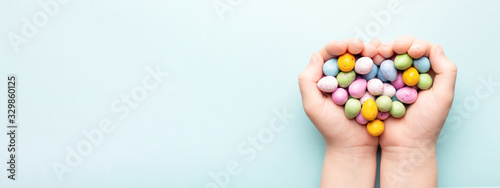 Child hands with Easter candies on blue background.
