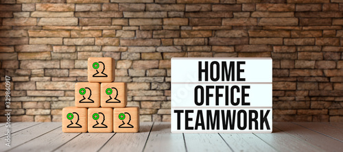 Plakat cubes with person-symbols stacked as a pyramid and lightbox with text HOME OFFICE TEAMWORK in front of a brick wall