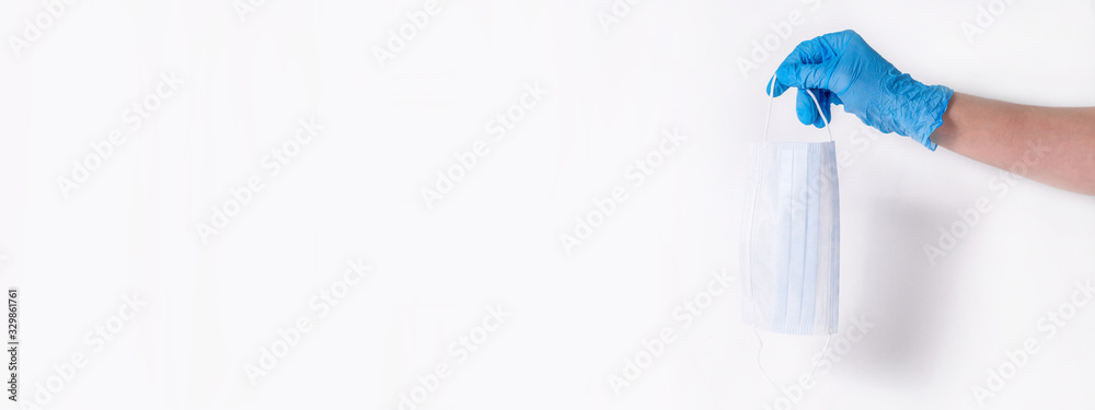 Personal protection against colds and viruses. A medical worker's hand in blue gloves drops a protective mask on a white background. The concept of maintaining health during the flu season. Copy space Personal protection against colds and viruses. A medical worker's hand in blue gloves drops a protective mask on a white background. The concept of maintaining health during the flu season. Copy space