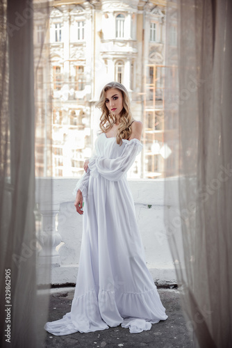 Fashion beauty bride in a long white dress on the terrace against the backdrop of the city. The perfect look for a modern bride.