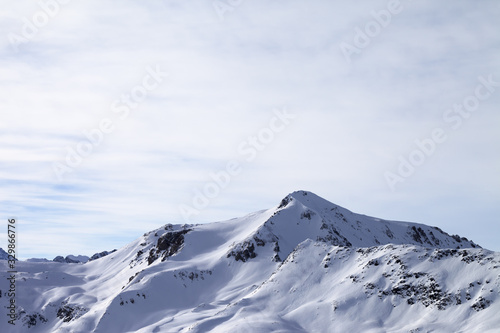 Sunlit snowy slopes in high winter mountains and cloudy sky at morning