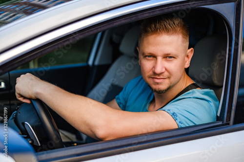 Young attractive driving man in white car, outdoors