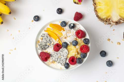 Healthy breakfast Smoothie bowl with mango, pineapple, dragon fruit, blueberries, raspberries and coconut. Tasty summer breakfast.