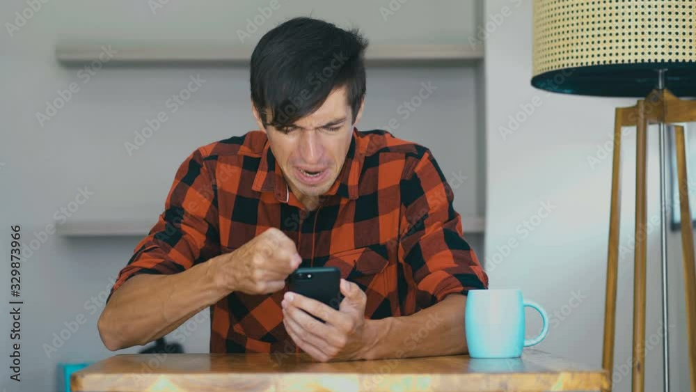 Angry Man Using Mobile phone at home. Frustrated entrepreneur is angry with the message that he read in the smartphone. Stressed businessman uses smartphone.