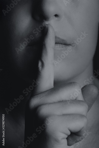 Conceptual monochrome image of woman holding finger to her lips keep quiet