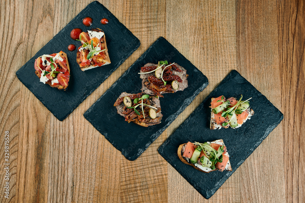 Assorted different bruschettas set. Italian appetizer in front of the main course. Bruschetta with roast beef, tomato salsa and salmon on a wooden background. Assorted different bruschettas set. Italian appetizer in front of the main course. Bruschetta with roast beef, tomato salsa and salmon on a wooden background.