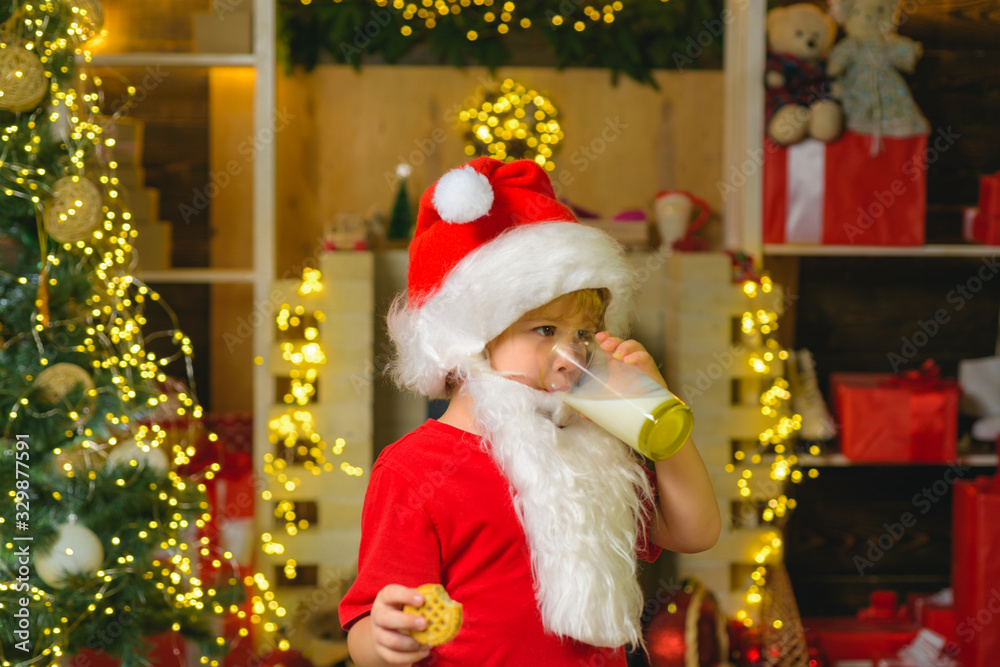 Portrait of Santa Claus Drinking milk from glass and holding cookies. Little Santa Claus kid with beard and mustache. Santa boy in Santa hat. Christmas for kid. Portrait of Santa Claus Drinking milk from glass and holding cookies. Little Santa Claus kid with beard and mustache. Santa boy in Santa hat. Christmas for kid.