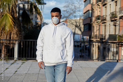 Sick young man standing on the street wearing protective facial mask against transmissible infectious diseases and as protection against the flu or coronavirus in public place.