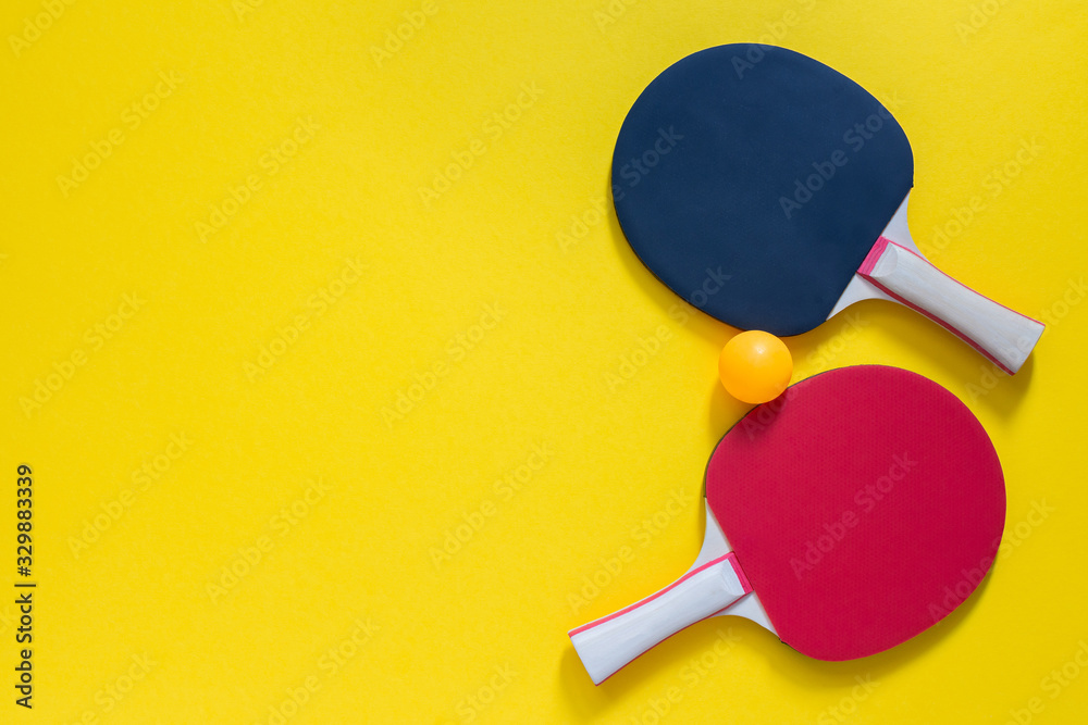 Red and black tennis ping pong rackets and orange ball isolated on a yellow background, sport equipment for table tennis Red and black tennis ping pong rackets and orange ball isolated on a yellow background, sport equipment for table tennis