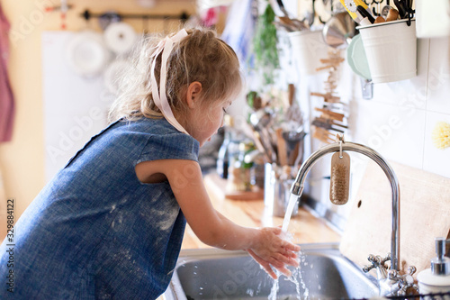 Kid washing hands at home under water tap. Cute child girl in flour after cooking in cozy home kitchen. Infection prevention. Avoid spreading viruses and germs.