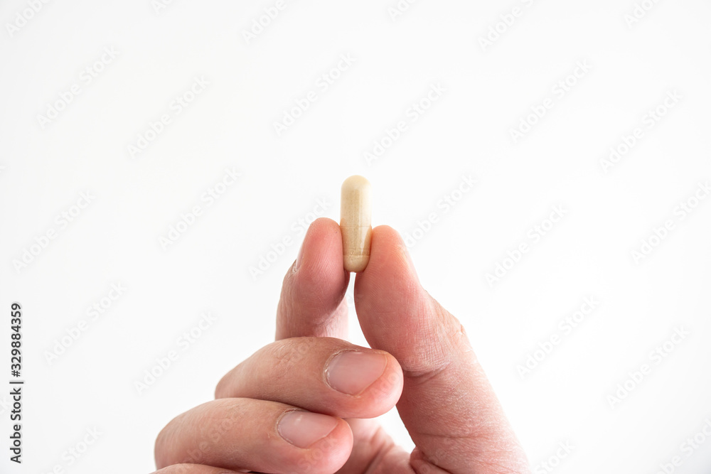 Nondescript medical pill held between fingers by Caucasian male hands close up shot isolated on white Nondescript medical pill held between fingers by Caucasian male hands close up shot isolated on white