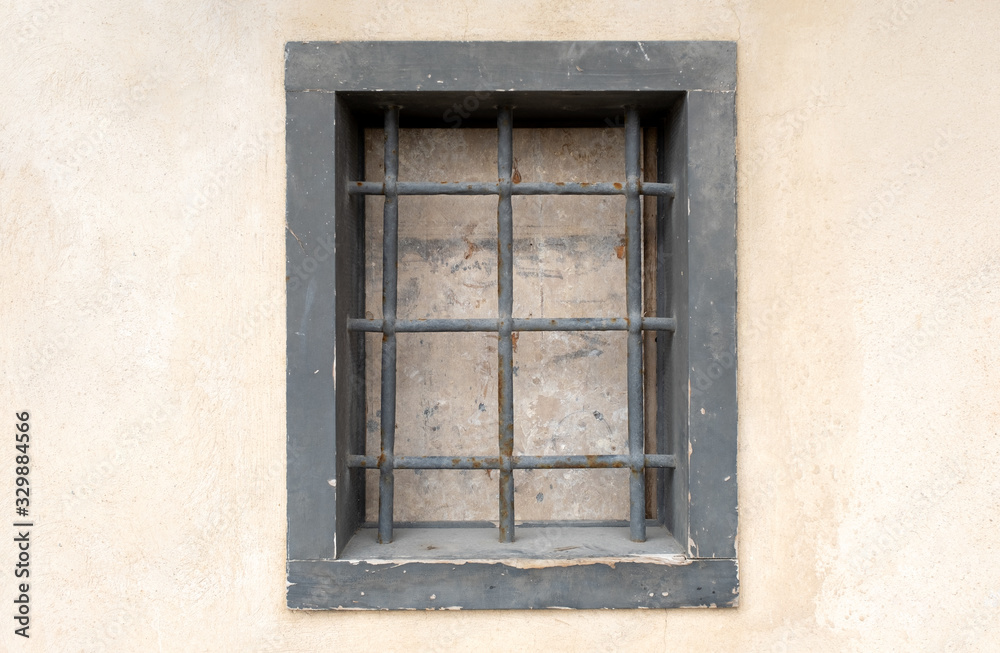 window with bars in the old city. there is one window on the wall which is closed and with a strong grating. prison in the city
