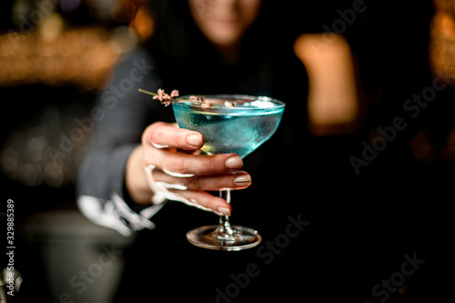 woman bartender holds blue cocktail on outstretched hand