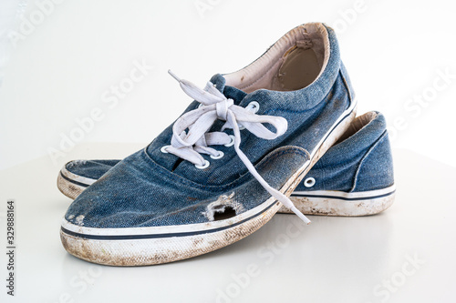 Pair or very badly worn out dirty blue casual leisure shoes with holes in them