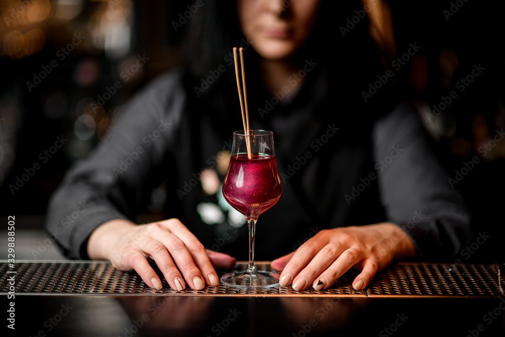 Cool pink cocktail in glass decorated with two sticks standing on bar.
