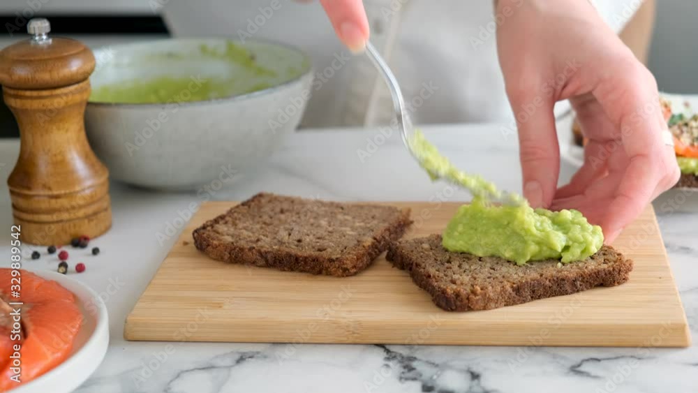 Spreading avocado on rye bread. Woman hands prepares healthy vegan