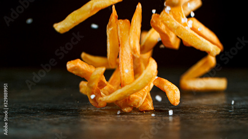 Freeze Motion Shot of Falling Fresh French Fries on Wooden Table and Adding Salt