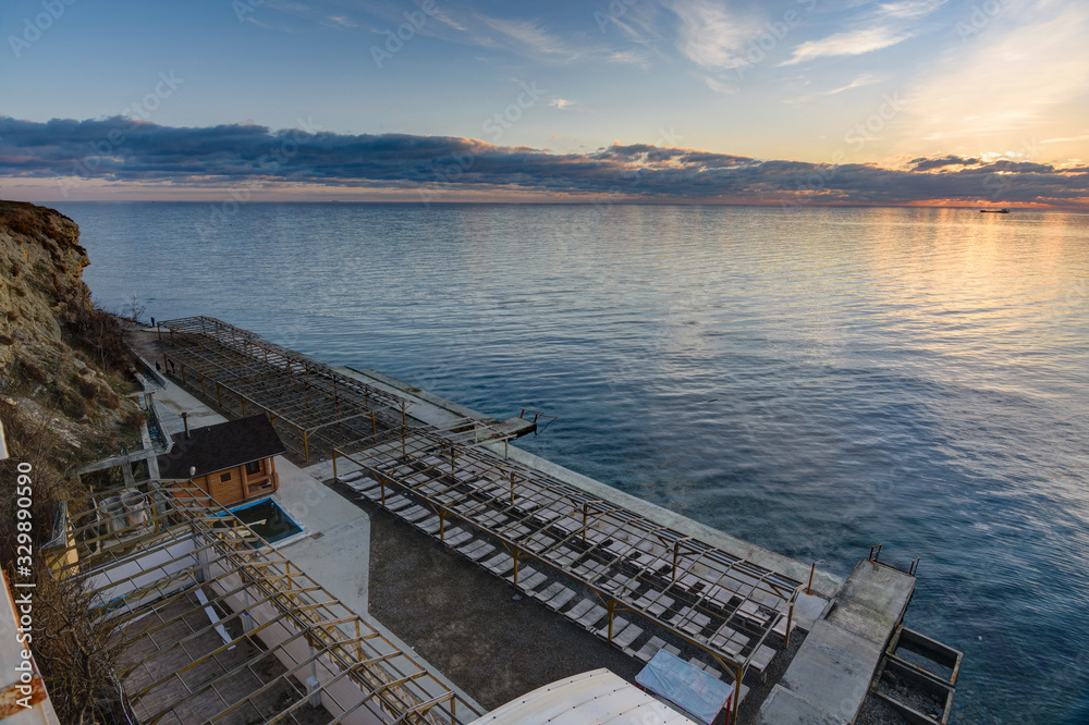Fototapeta premium Sunset view on an empty sunlounge beach on a rocky sea shore