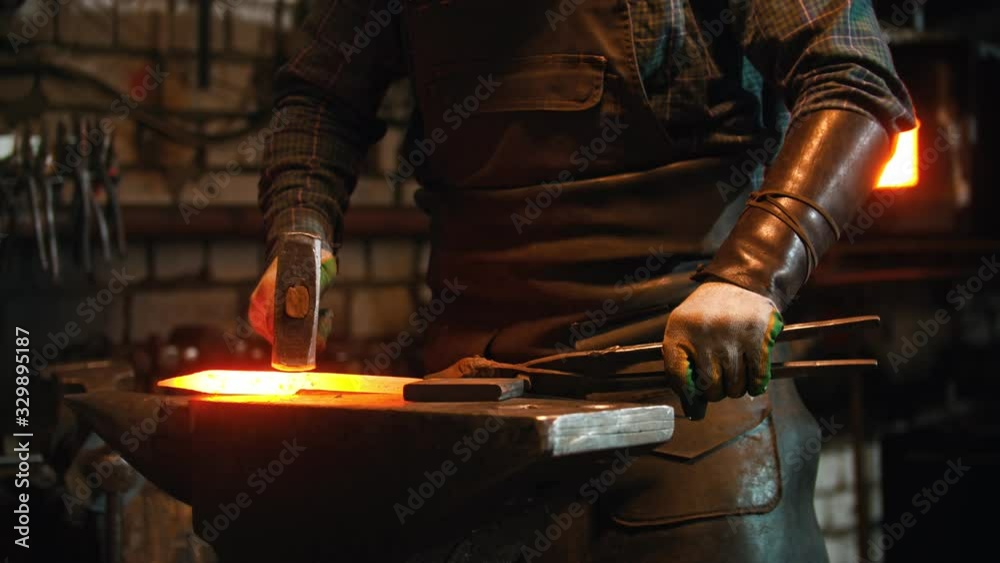 Blacksmith working in the workshop - man heating up the longer piece of metal in the furnace and hitting it with a hammer Blacksmith working in the workshop - man heating up the longer piece of metal in the furnace and hitting it with a hammer