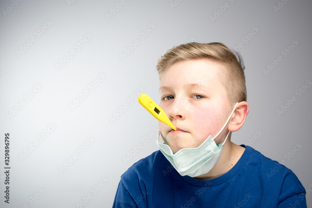 A child with a thermometer in his mouth. A child in an antiviral mask.