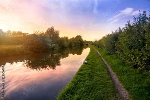Looking along the tow path of the Grand Union Canal in Northamptonshire with a colorful sunset behind the trees on the opposite bank with the orange and red sky reflecting in the still water photo
