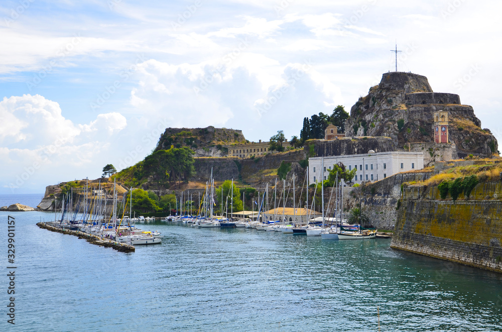 Mandraki Harbor and beach, with sailing boats overseen by the old fort on the hill above, in Corfu