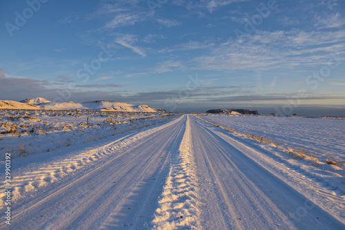 Looking down a straight road in a snow covered landscape in southern Iceland   late afternoon in mid-winter