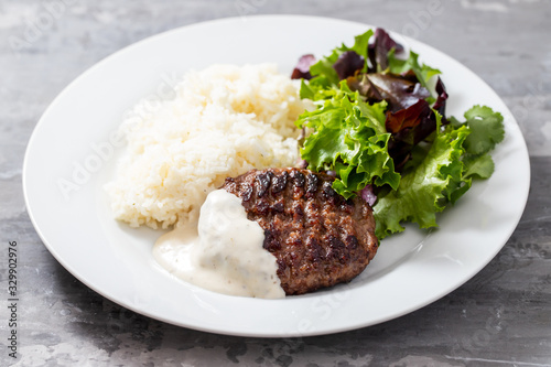 grilled hamburger with sauce, boiled rice and fresh salad on white plate